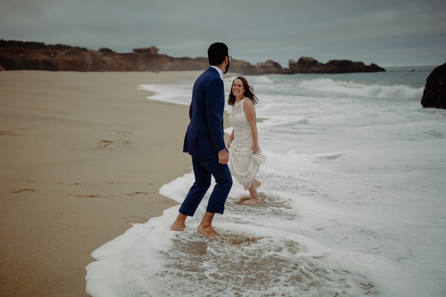 A couple is running in the water at the beach after their elopement in Big Sur.