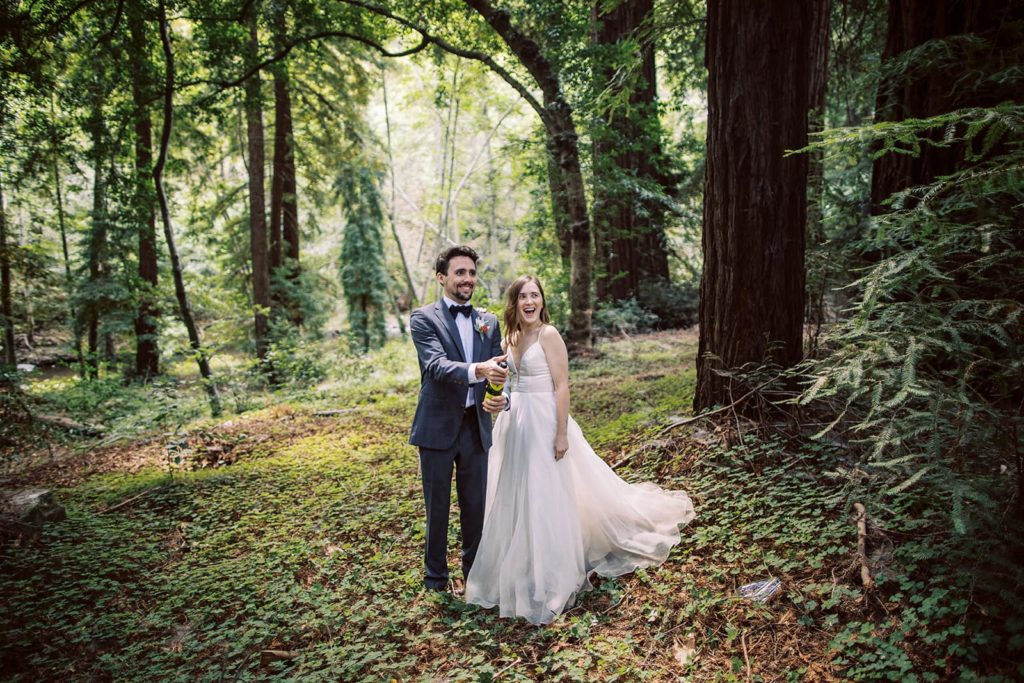 A couple popping champagne in the redwood forest in Big Sur to celebrate their elopement day.