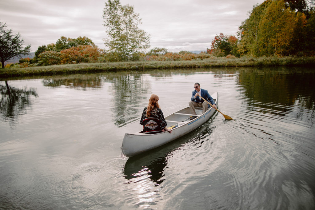 A couple is kayaking on a lake in Europe, wearing their elopement attire. 