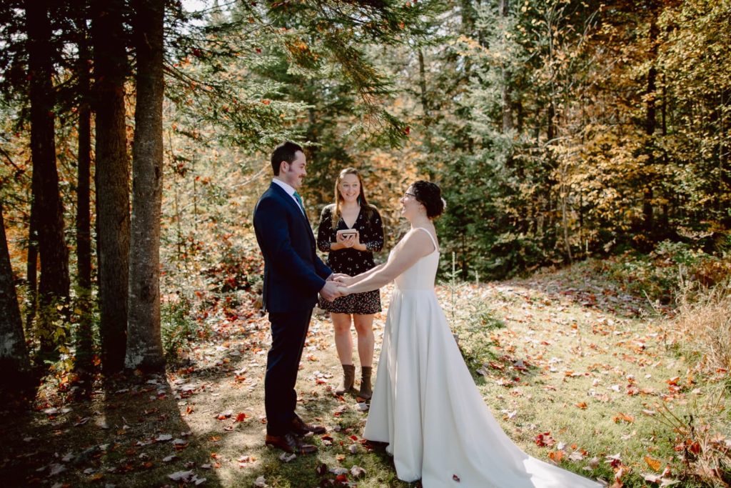 Couple Standing in the Woods of Vermont Saying Vows with Fall Foliage Colors 