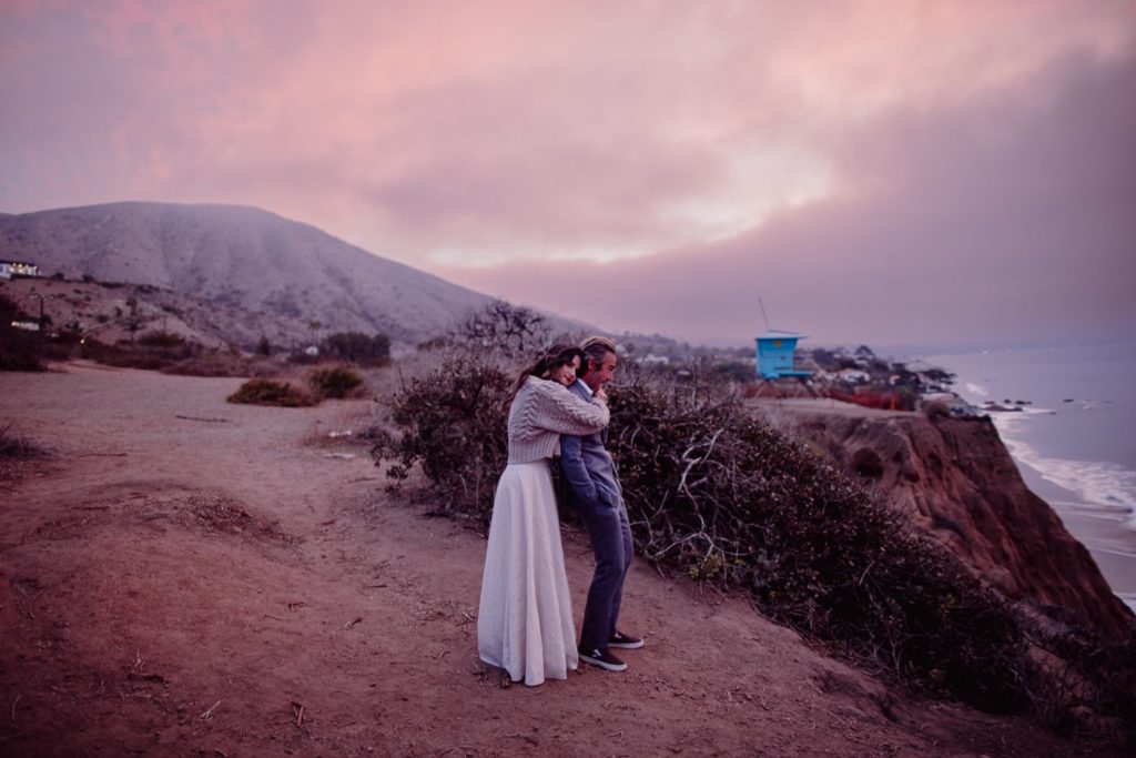 Couple Standing on Cliff in Malibu at Sunrise Hugging with a Pink Sky