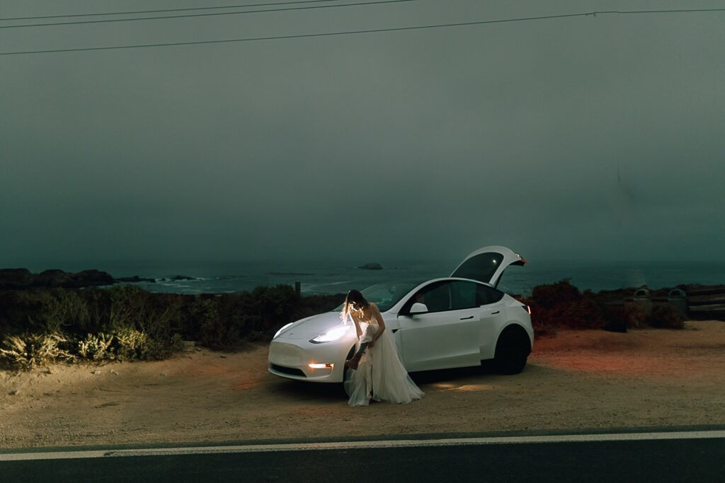 Bride getting ready in front of her Tesla on the side of the road in Big Sur