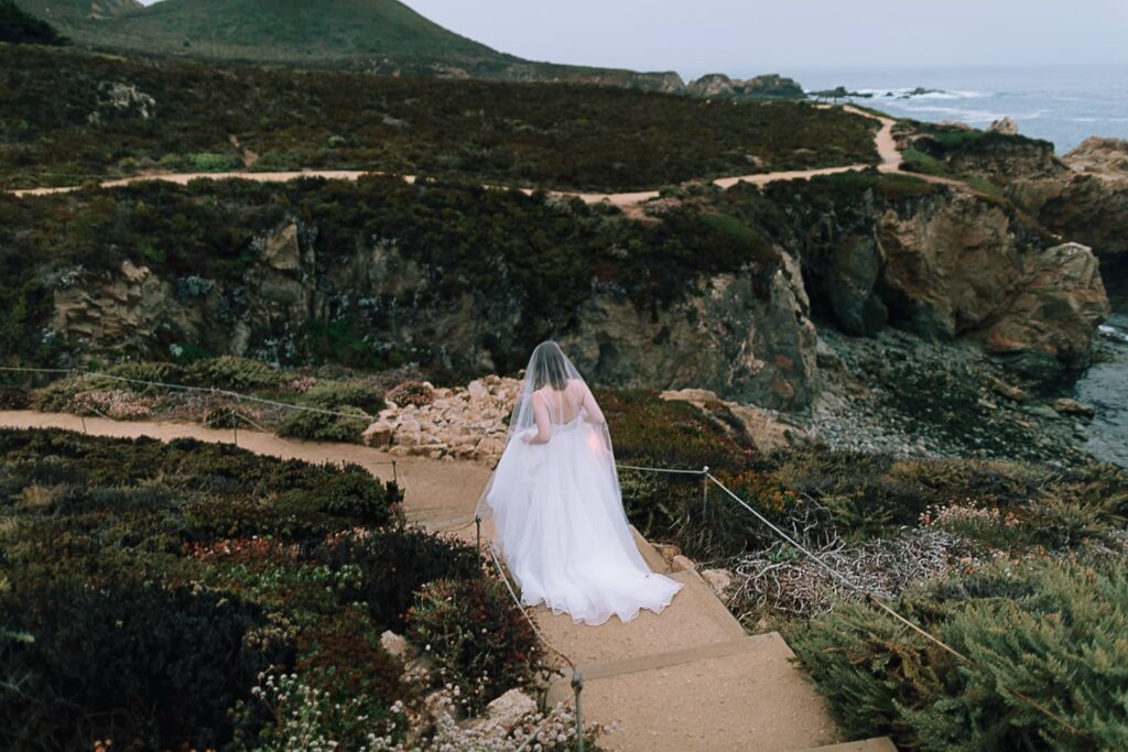 Bride in a long veil and Sarah Seven wedding dress walking down the coast of Big Sur