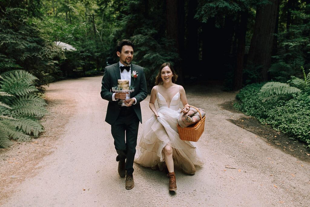 Couple waking through the Redwood forest holding wedding cake on their wedding day